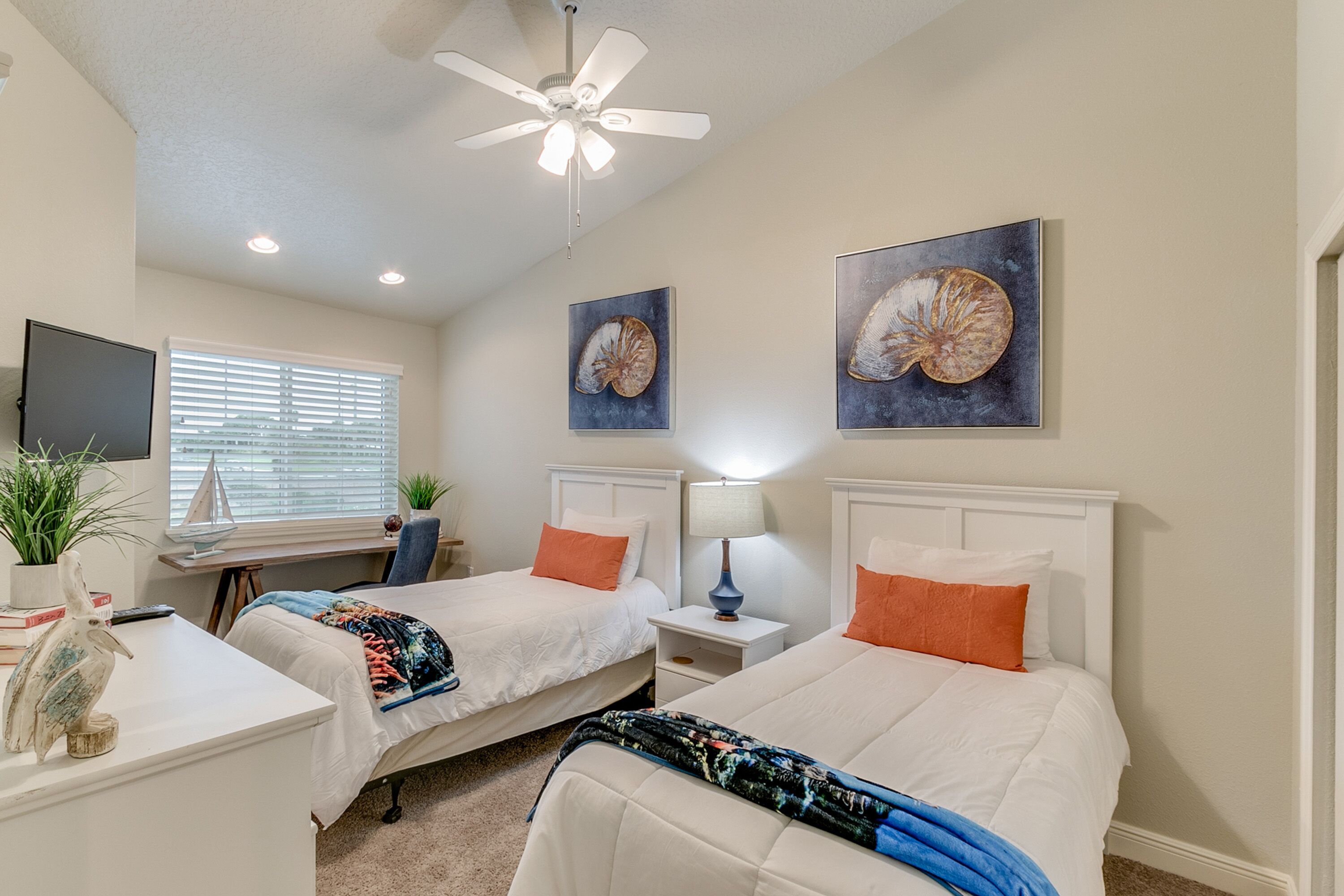 A bedroom with two beds, a desk, a chair, a TV, and artwork on the walls.