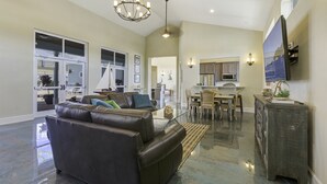 A spacious living room with a leather sofa, a dining area with a wooden table and chairs, and a kitchen with modern appliances.