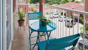 A balcony with a table and chairs, potted plants, and a view of a residential area with cars and houses. - New Kingston Guest Apt at Fairway (Kingston)