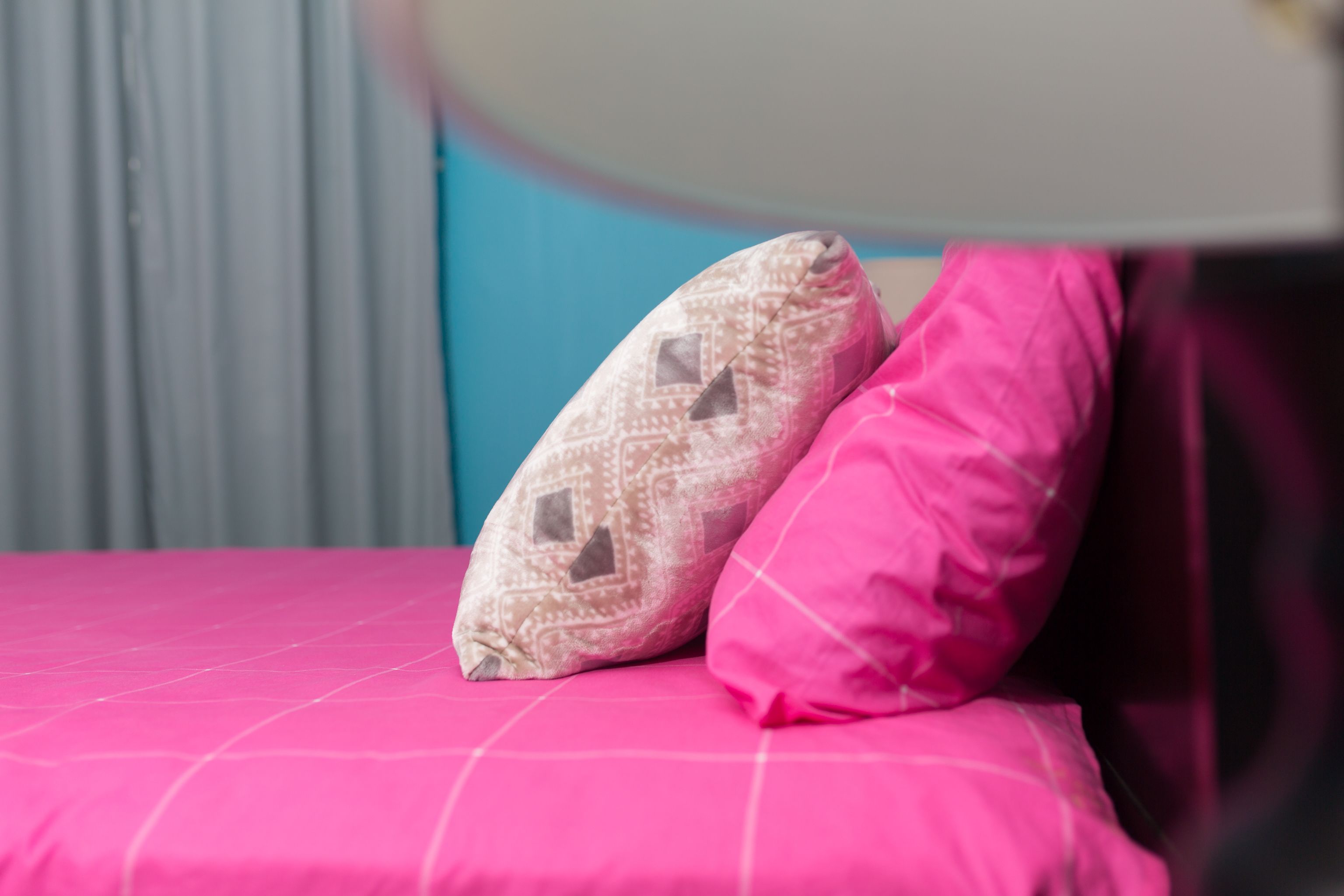 Un lit avec une couvre-lit rose et deux oreillers, l’un à motifs et l’autre uni, également rose.