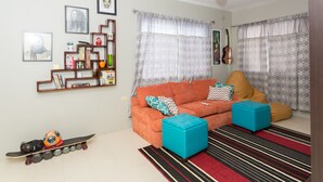 A living room with a sofa, ottomans, a striped rug, a ceiling fan, and a wall with framed pictures. - The Hellshire Beach House (Hellshire)
