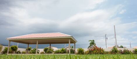 A covered pavilion in a grassy area with a view of the ocean and cloudy sky.