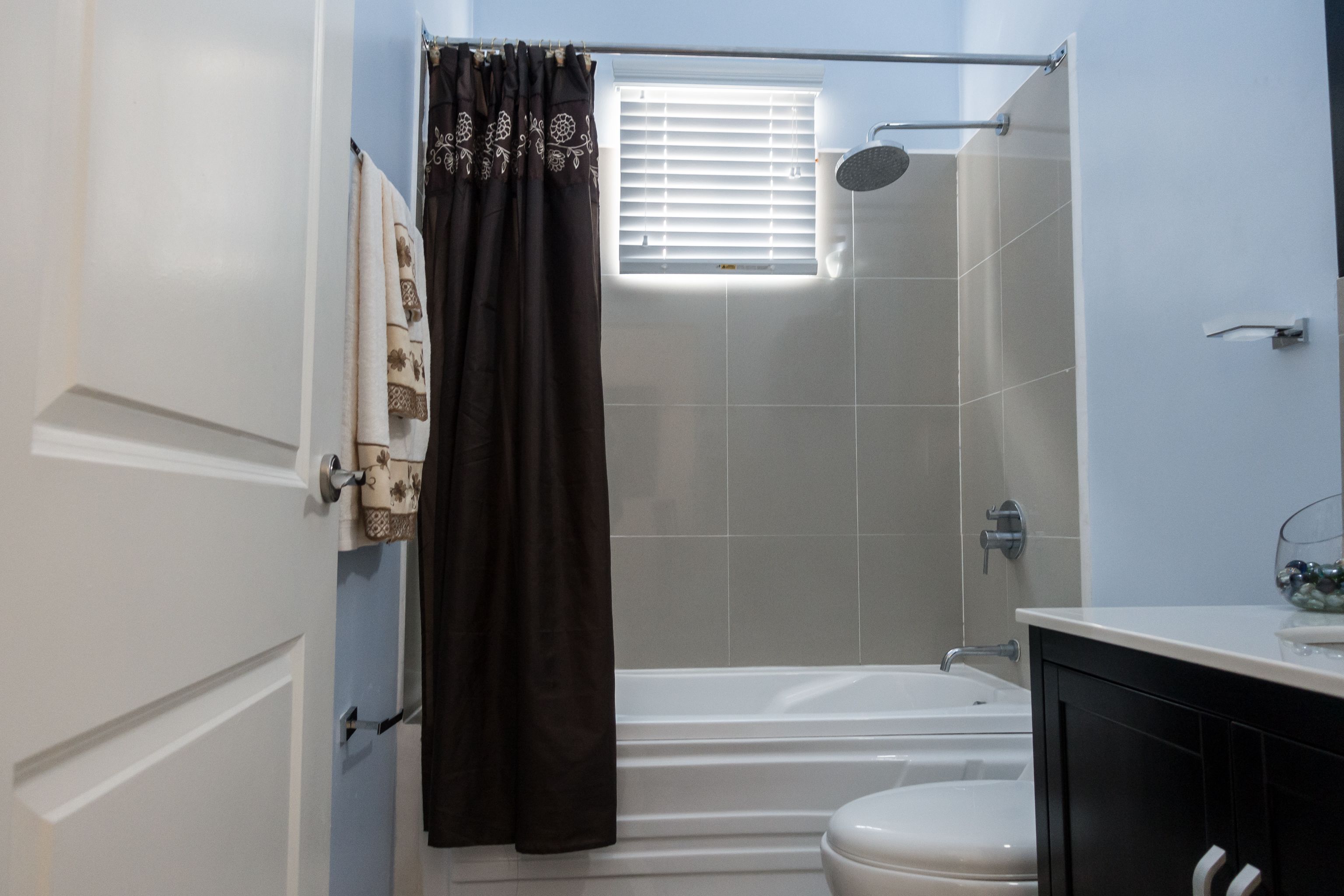 Une salle de bain avec une baignoire, des toilettes et une fenêtre avec des stores.
