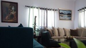 A living room with a sofa, a glass coffee table, a potted plant, and two framed pictures on the wall. - The Country Club Villa I (Kingston)