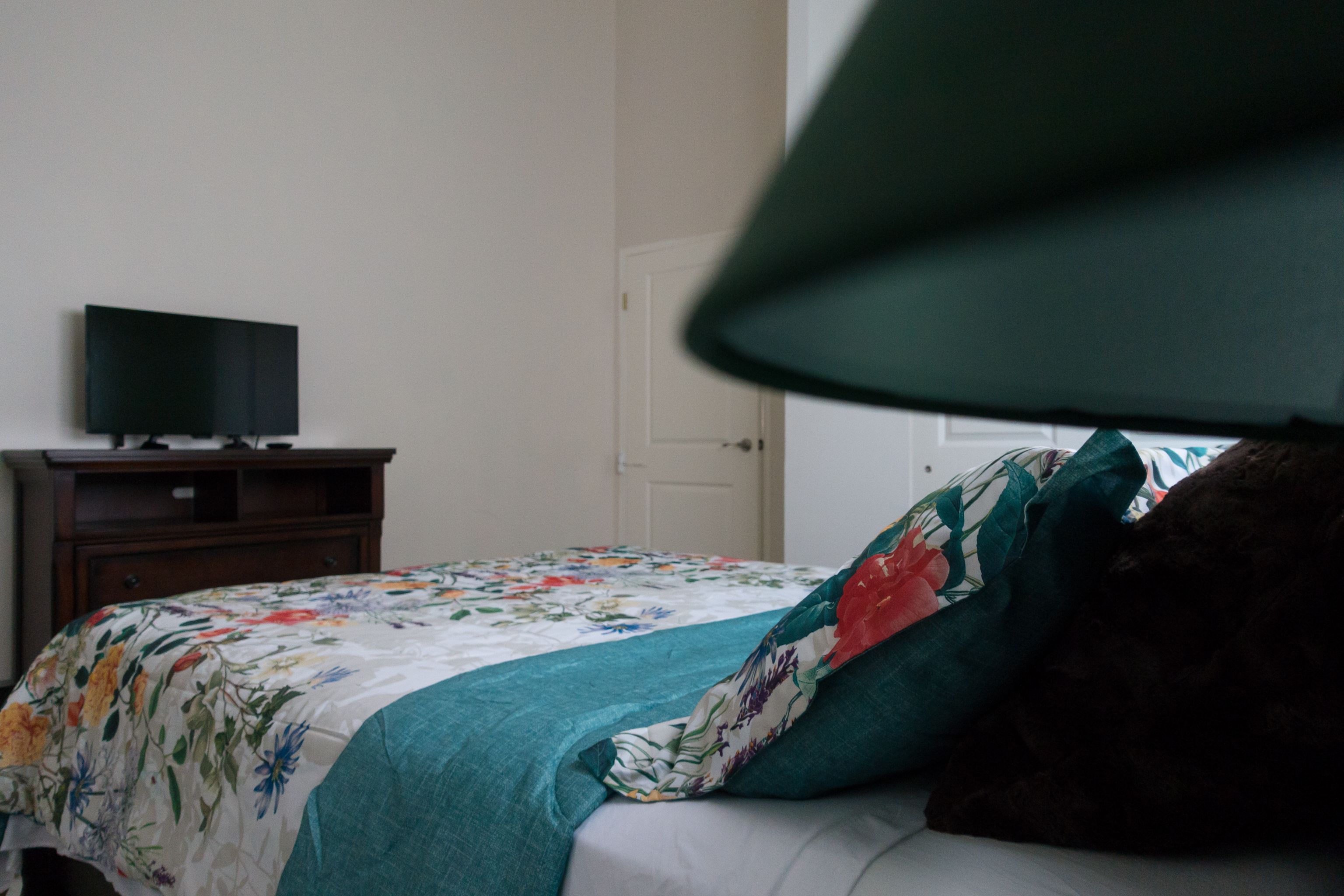 Quarto com cama, televisão em móvel e porta ao fundo.