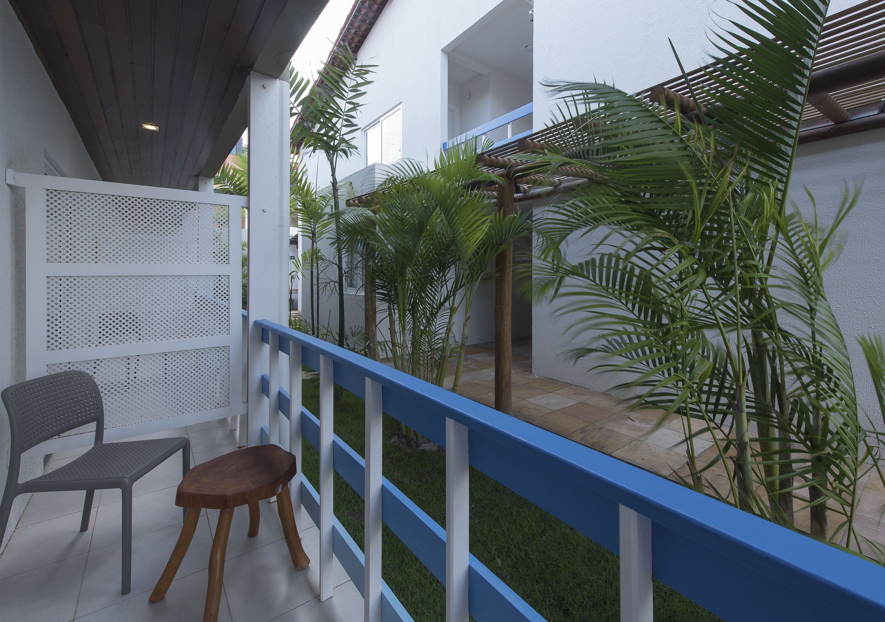 Un balcone con una sedia bianca, uno sgabello di legno e una ringhiera blu.