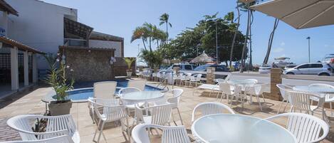 An outdoor patio with white plastic chairs and tables, a swimming pool, and a view of the ocean.