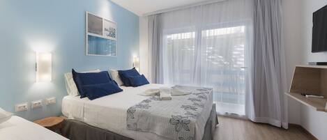 A hotel room with a bed, a bedside table, a TV, and a window with curtains.