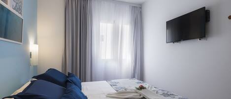 A hotel room with a bed, a flat-screen TV mounted on the wall, and a window with curtains.