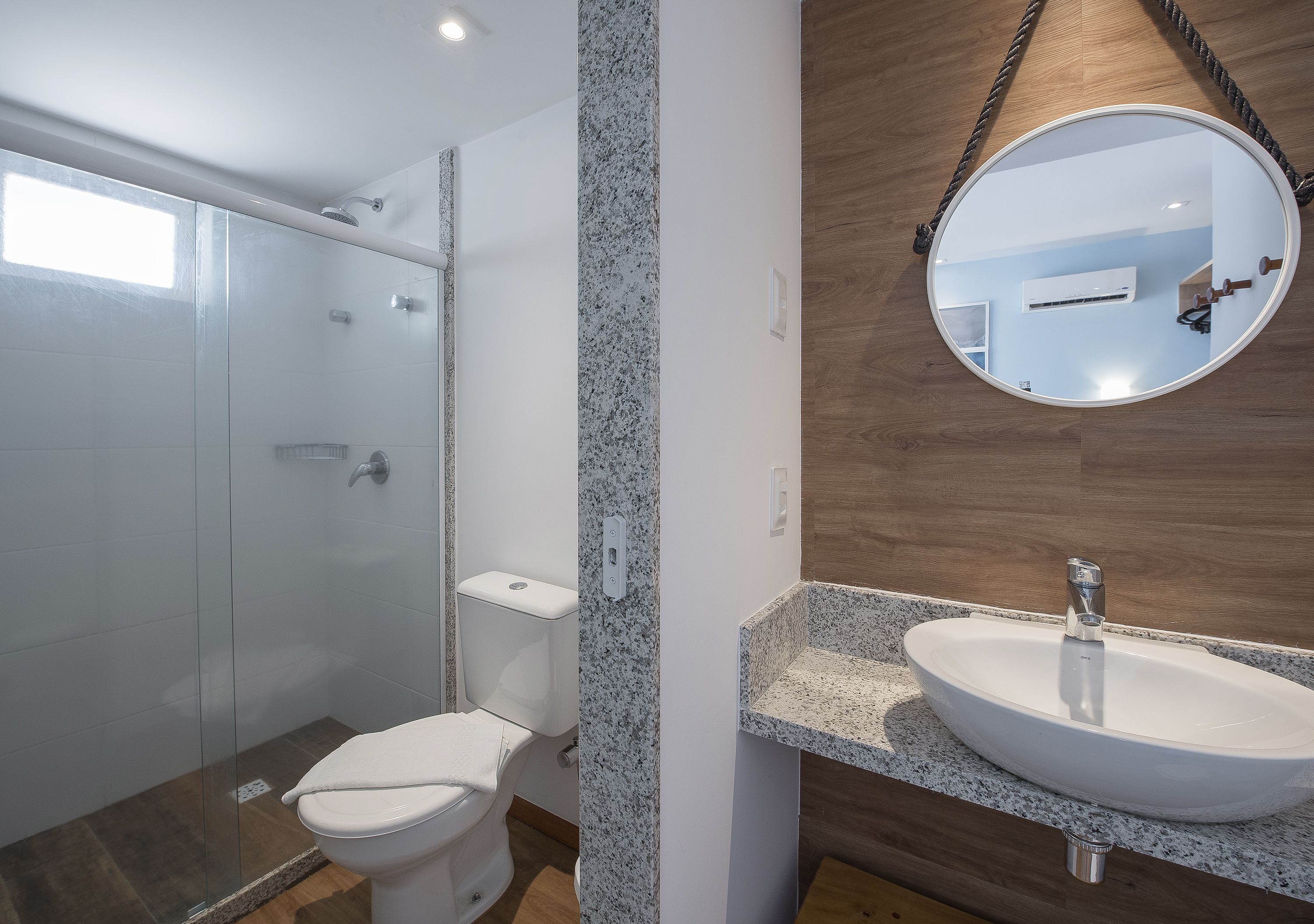 A modern bathroom with a glass-enclosed shower, a white toilet, and a granite countertop sink.
