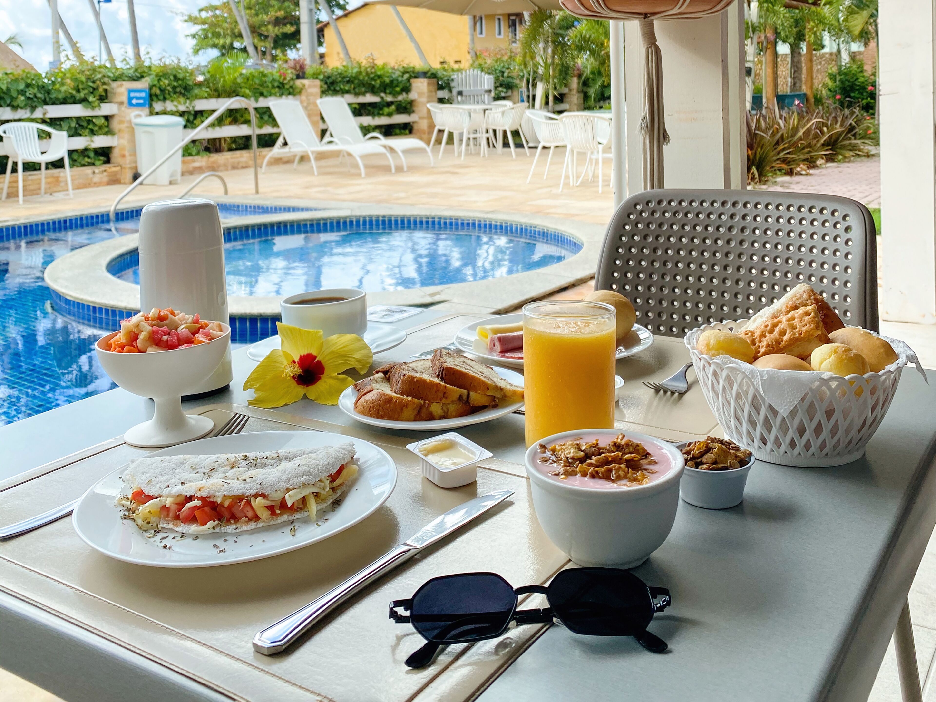 Una mesa de desayuno con vista a la piscina, que incluye un bol de fruta, una taza de café, tostadas y un vaso de zumo de naranja.