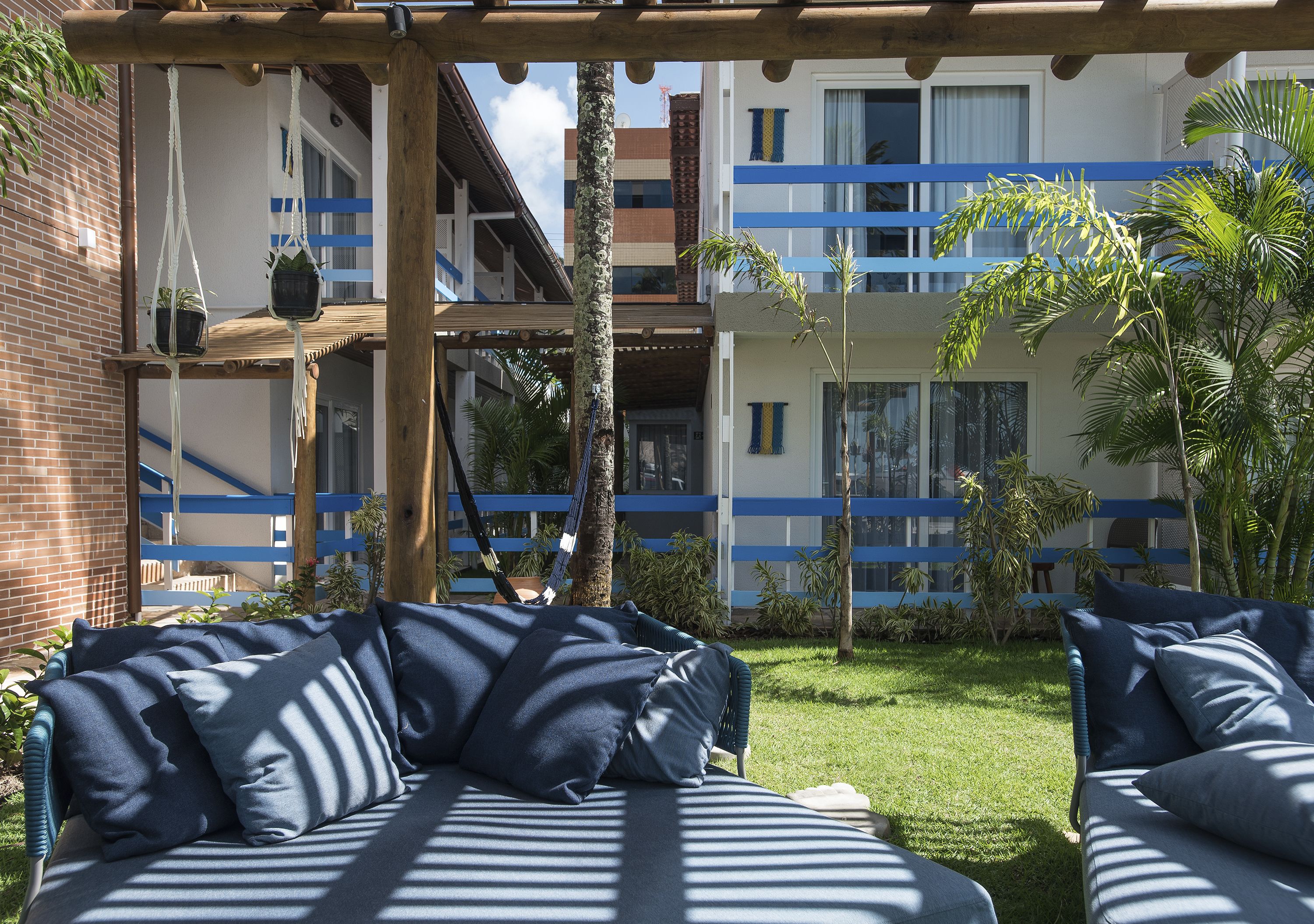 Un patio con sofá y sillas, una pérgola de madera y un edificio con detalles azules.