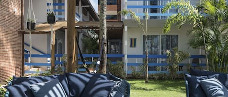 Un patio con sofá y sillas, una pérgola de madera y un edificio con detalles azules.