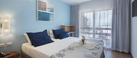 Ein Hotelzimmer mit einem Bett, einem Nachttisch mit Telefon, einer Wand-Klimaanlage und einem Fenster mit Vorhängen.