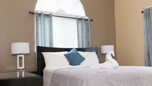 A hotel room with a bed, two bedside lamps, a window with curtains, and a swan-shaped pillow. - The Country Club Villa II (Kingston)