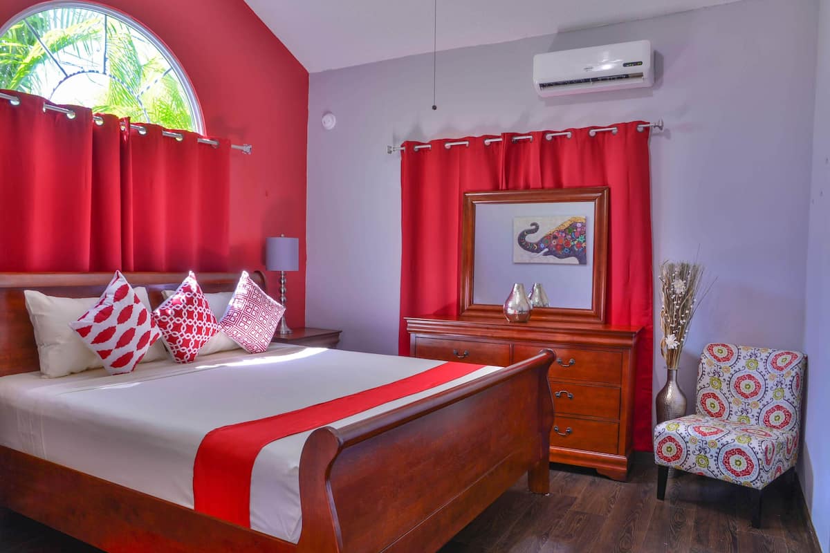Un dormitorio con una cama de madera, cortinas rojas, un espejo, un aparador y una silla.