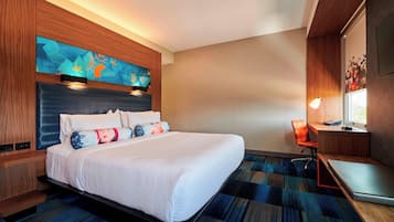 A modern hotel room with a large bed, a desk with a laptop, a chair, and a painting on the wall.