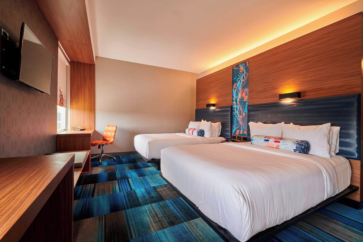 A hotel room with two beds, a desk, and a chair.