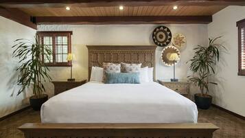 A bedroom with a wooden bed, two nightstands, a window with blinds, and two potted plants.