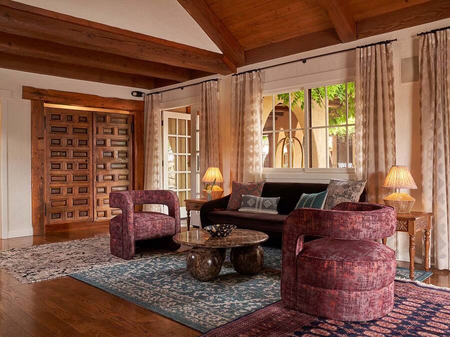 A cozy living room with a wooden ceiling, a patterned rug, a sofa, two armchairs, and a coffee table.