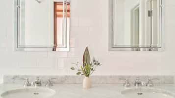 A bathroom with two sinks, each with a mirror above. There is a vase with a plant in the center of the sink area.