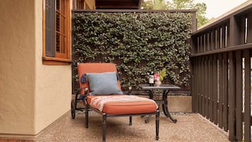 Un espacio al aire libre con acceso para sillas de ruedas, que incluye una silla acolchada y una mesita pequeña, una pared decorativa con plantas trepadoras y una valla de madera.
