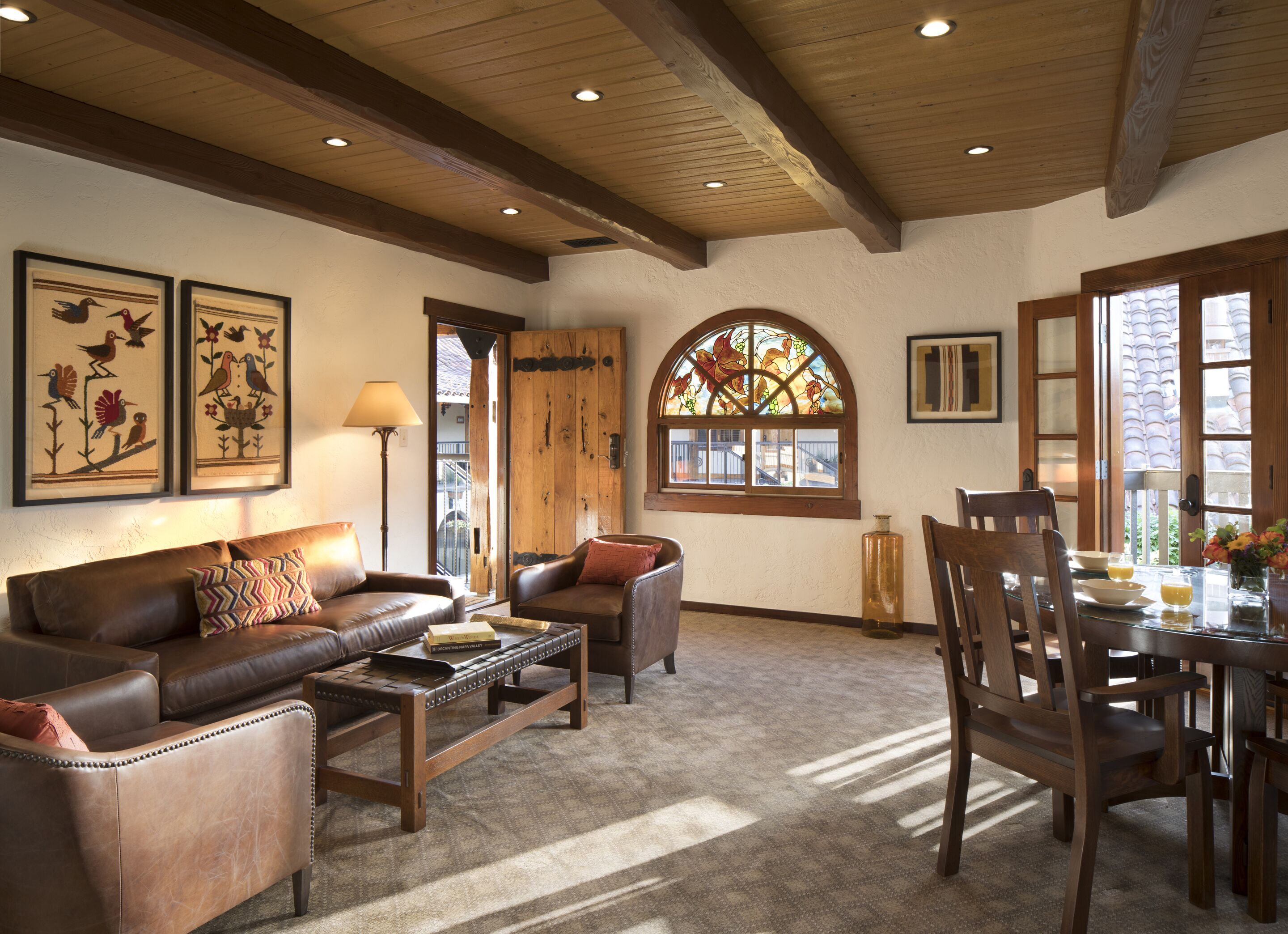 A cozy living room with a brown leather sofa, a wooden coffee table, and a dining area with a wooden table and chairs.