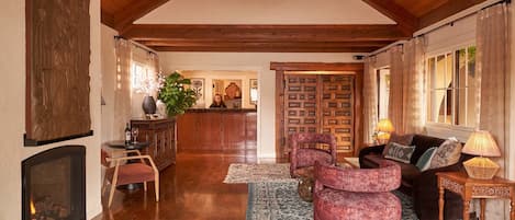 A spacious living room with a fireplace, wooden beams, a chandelier, and a cozy seating area.