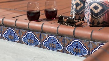 A tiled patio with two glasses of red wine, a pair of sunglasses, and a patterned cushion.