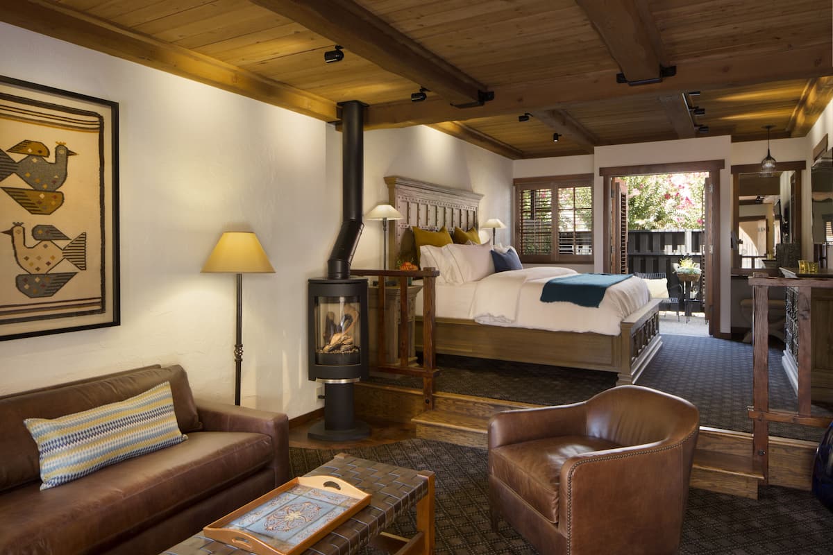 A cozy room with a bed, a sofa, a chair, a table, and a fireplace.