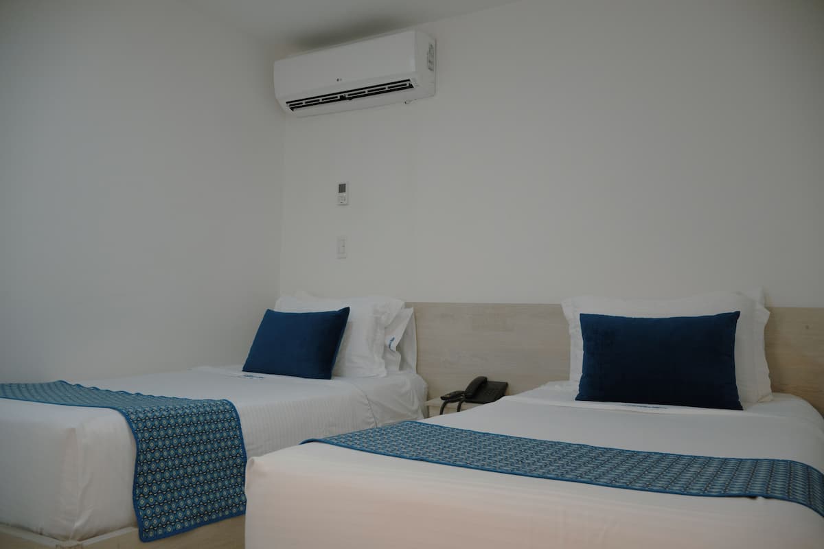 Ein Hotelzimmer mit zwei Betten, jeweils mit einer blau gemusterten Tagesdecke, weißen Kissen und einem beige farbenen Kopfteil.