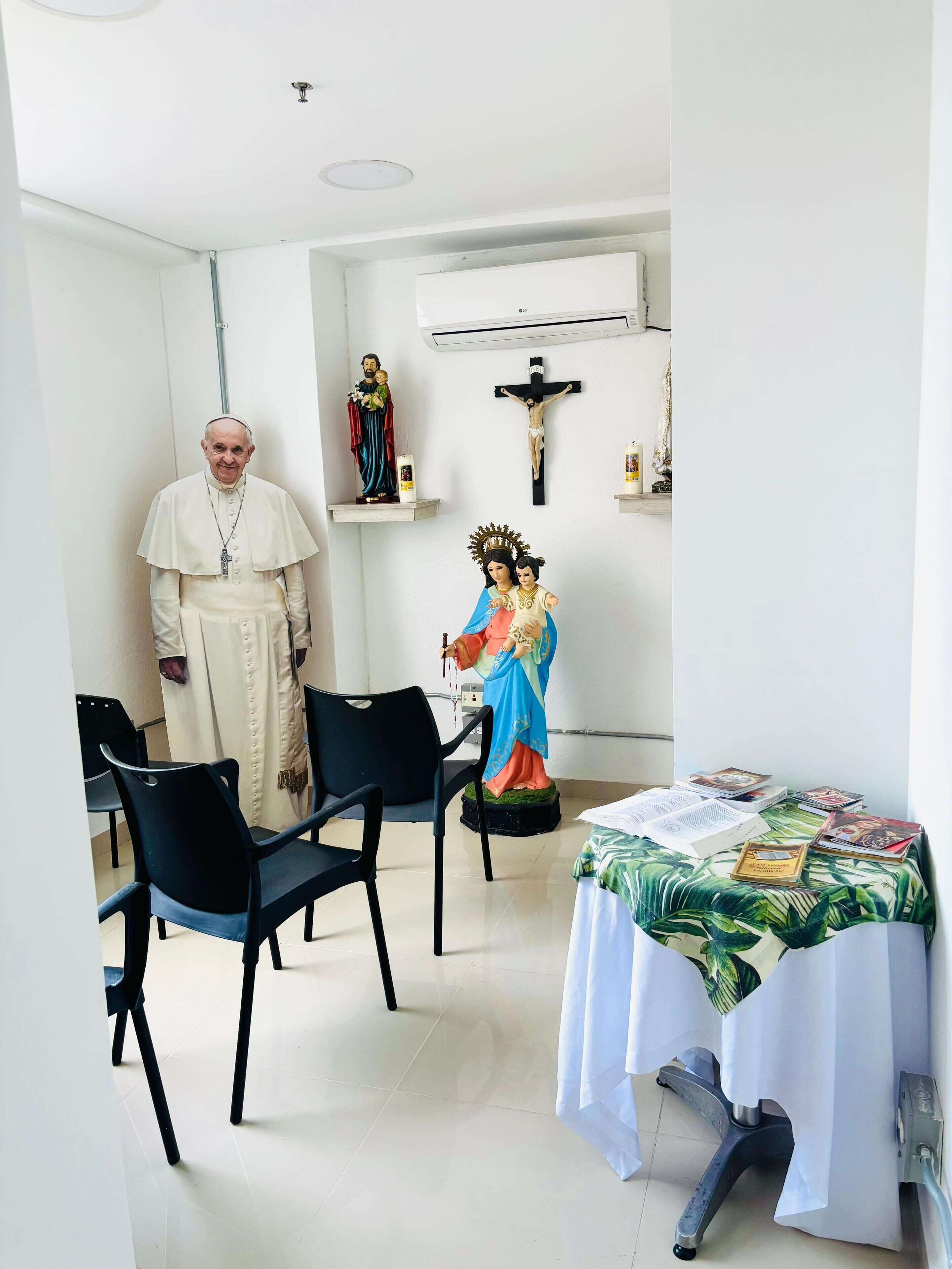 Una habitación con cama, sillas, una estatua y un crucifijo.