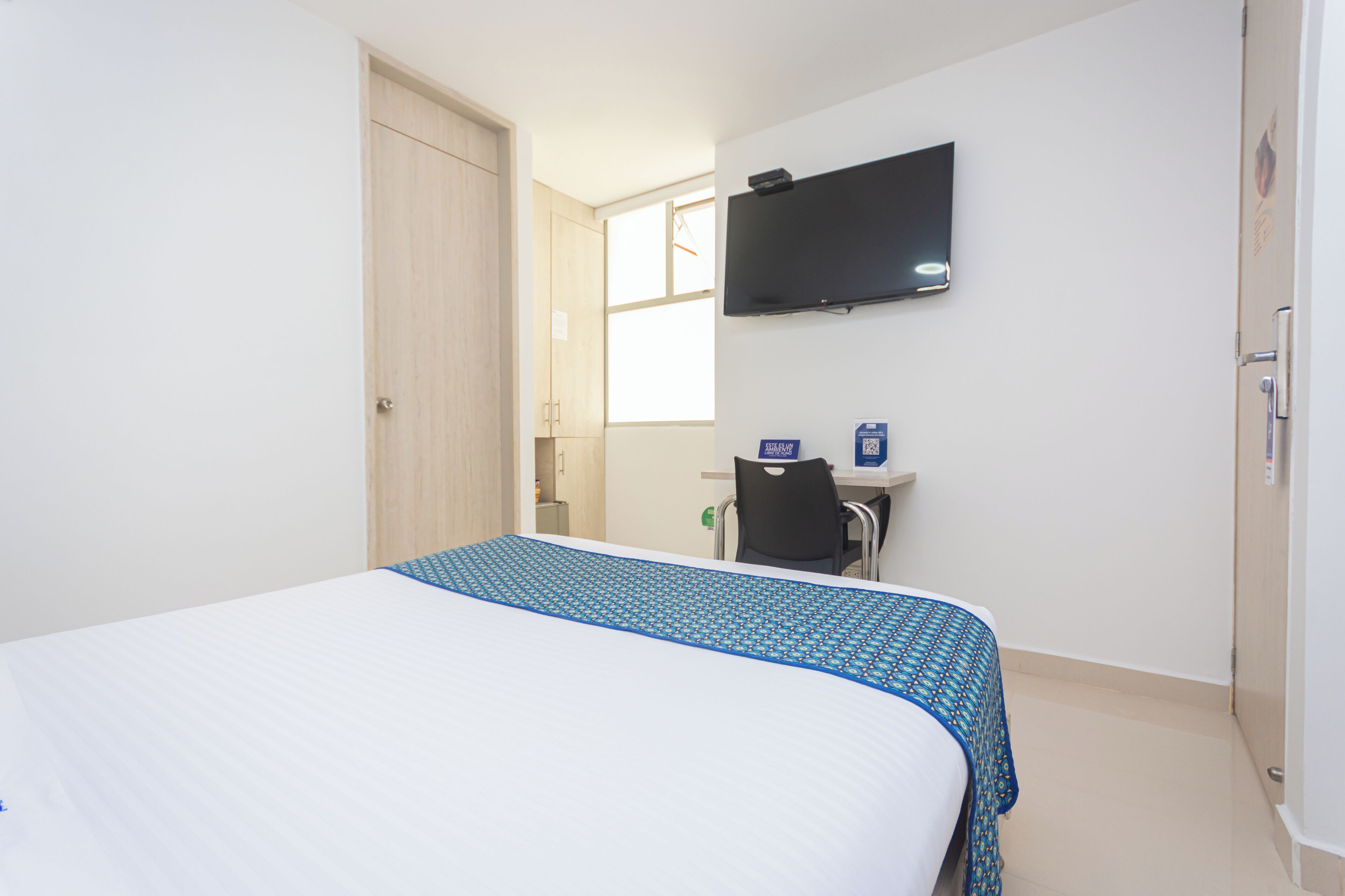 Ein Hotelzimmer mit Bett, Schreibtisch, Stuhl, Fernseher und Fenster.