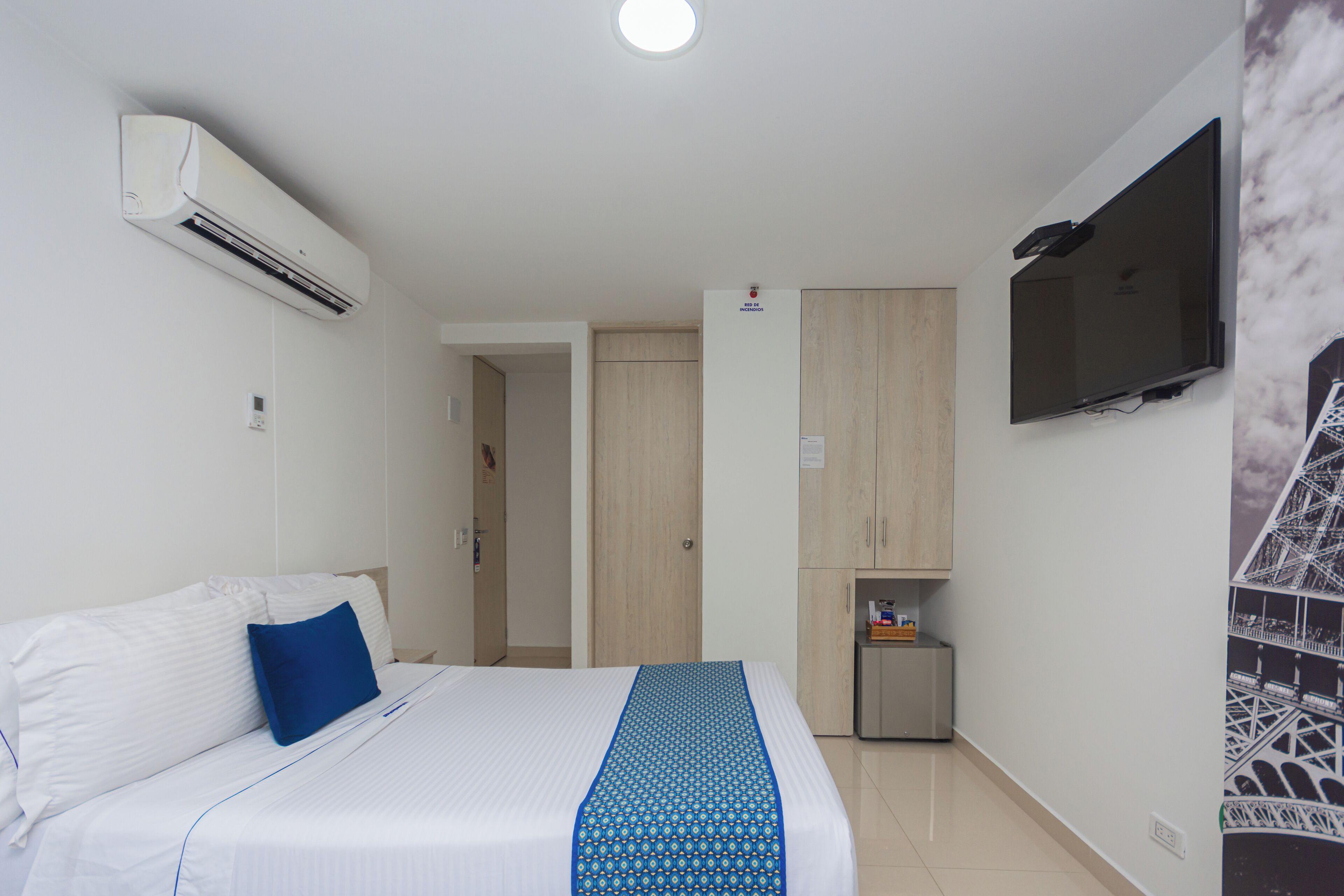 A hotel room with a bed, a TV mounted on the wall, and a small cabinet.