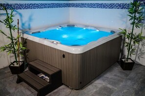 Ein Whirlpool mit Holzeinfassung, umgeben von Kübelbambuspflanzen, mit einer kleinen Holzbank davor.