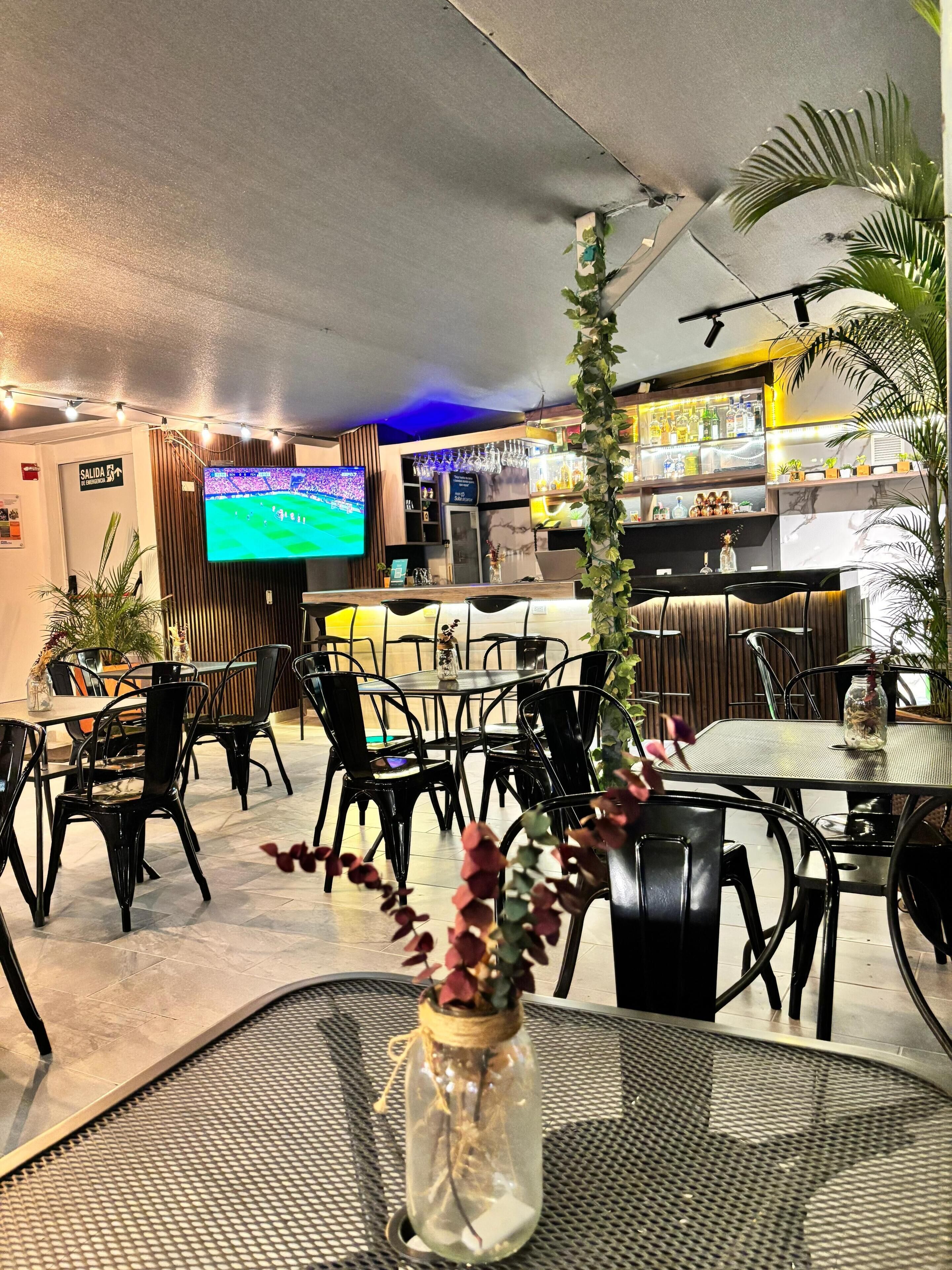 A restaurant with a bar area, tables, chairs, a television screen, and decorative plants.