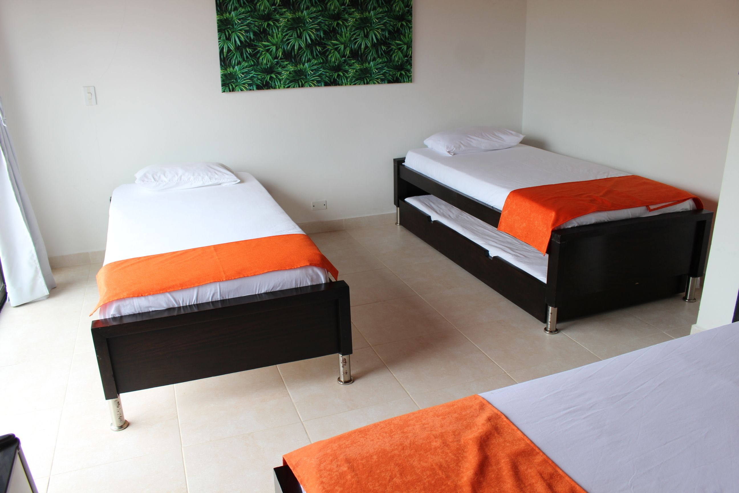Two single beds with orange and white bedding, a green leaf-patterned wall hanging, and a tiled floor.