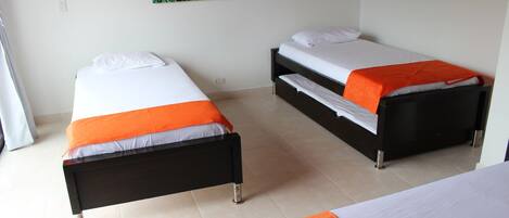 Two single beds with orange and white bedding, a green leaf-patterned wall hanging, and a tiled floor.
