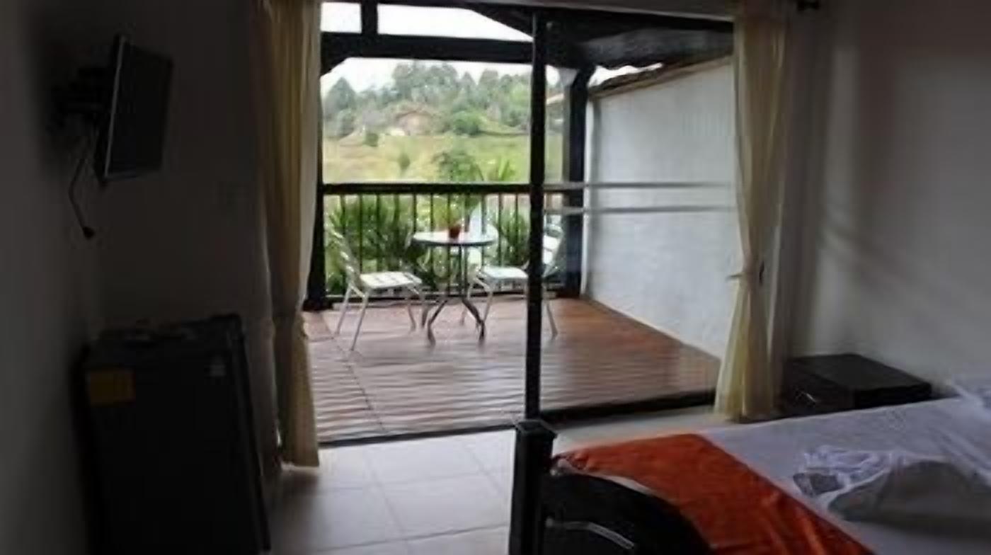 A room with a bed, a small table, and a balcony with chairs.