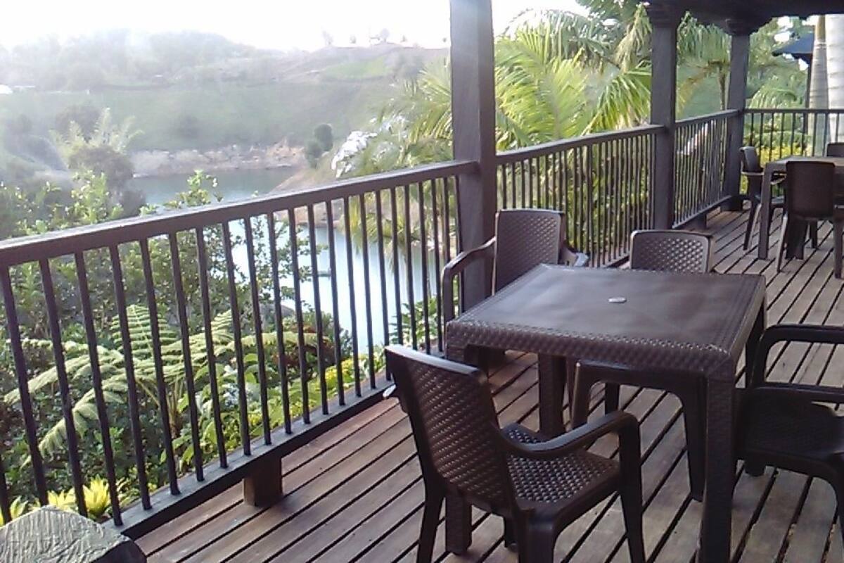 A wooden deck with a table and chairs, overlooking a body of water and greenery.