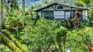 A two-story house with a balcony, surrounded by lush greenery and hills in the background. - Hotel Santa Maria de las Aguas Peñol (El Peñol)
