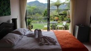 A bedroom with a bed, a view of a garden and mountains through a large window. - Hotel Santa Maria de las Aguas Peñol (El Peñol)