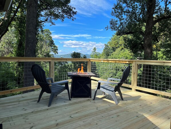 A wooden deck with two chairs and a table, surrounded by a metal fence and trees.