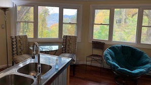 Una cocina con pileta, dos sillas, una mesa y ventanas amplias que dan a árboles y montañas.