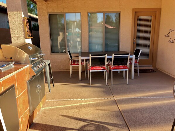 An outdoor patio with a grill, dining table, and chairs.