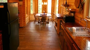 A wooden cabin interior with a kitchen, dining area, and a large window.