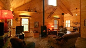 A cozy log cabin interior with a fireplace, wooden walls, a television, and a comfortable seating area.