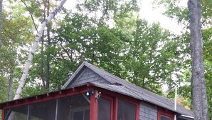 Eine kleine Holzhütte mit roter Tür und Fenstern, einer Holztreppe und einem Gitternzaun.