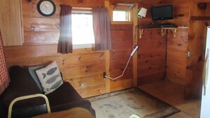 Ein Holzblockbau-Innenraum mit einer Couch, einem Fernseher, einer Uhr und einem Fenster mit Vorhängen.