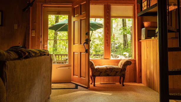 A wooden cabin interior with a bench, a door leading to a balcony, and a window with an umbrella.